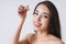 Beauty portrait of happy smiling asian woman with dark long hair with pipette with organic oil on clean fresh skin face and hands