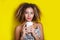 Beauty portrait of young african american woman with afro hairstyle. Girl posing with coffee on yellow background, looking at came