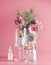 Beauty product setting with glass bell jar,  serum pipette bottles and flower bouquet at pink background. Healthy skin care