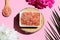 Beauty and spa concept. Pink himalayan salt on a wooden cut with palm leaf and peony flowers. Selective focus. Top view