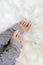 Beauty woman feet with french pedicure in grey knit warmers on white fur.