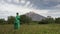 Beauty woman in green leather coat walking in summer forest against backdrop of mountain landscape