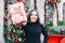 Beautyful young girl unpacks her box with a christmas gift. Woman with a gift in her hands stands on the background of Christmas d