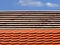 beaver tail brown clay roof tile installation on sloped roof. wooden lattice work. clear light blue sky.