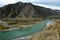 The bed of a beautiful turquoise river flowing through an autumnal valley at the foot of a high mountain