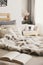 Bed with open book, pillows and fur coverlet in Scandi apartment interior with blurred background