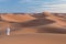 Bedouin on way through sandy desert. Beautiful sunset with big dunes on Sahara, Morocco. Silhouette nomad man.