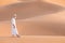 Bedouin on way through sandy desert. Beautiful sunset with big dunes on Sahara, Morocco. Silhouette nomad man.