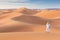 Bedouin on way through sandy desert. Beautiful sunset with big dunes on Sahara, Morocco. Silhouette nomad man.