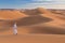 Bedouin on way through sandy desert. Beautiful sunset with big dunes on Sahara, Morocco. Silhouette nomad man.