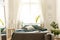Bedroom interior in nature colors with big bed, gray and green linen and pillows, fresh meadow flowers and a sunny window in the b