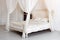 Bedroom in soft light colors. Big comfortable four poster double bed in elegant classic bedroom. Luxury elegant white with gold in