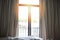 Bedroom window in the morning / sunlight through in room open curtains with balcony and nature tree on outside
