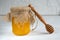 Bee honey in a glass jar decorated with burlap and wooden false on a white wooden background.