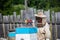 Bee master on apiary. Man in protective hat works with chimney in the beehive. Beekeeper examining bees on a bee farm on