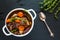 Beef Bourguignon in a white soup bowl on black stone background, top view. Stew with carrots, onions, mushrooms, bacon