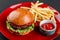 Beef burger and french fries with tomato sauce on red plate over dark background. Unhealthy food