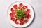 Beef carpaccio cold appetizer with parmesan, capers and arugula on white plate