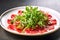 Beef carpaccio cold appetizer with parmesan, capers and arugula on white plate
