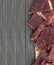 Beef jerky pieces on paper bag on wooden table, top view. Slices of spicy dry-cured meat