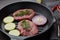 Beef steaks and cutting vegetables on grill pan on black slate background. Steak menu