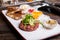 Beef tartare with arugula salad, crisp bread chips, sauces and snacks on white plate on the served restaurant table