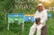 Beekeeper in protective clothing holding smoker while standing at apiary.