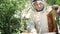 A beekeeper in a protective suit shakes the honey frame from bees with a brush. Pumping honey. Apiculture. Beekeeper