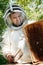 A beekeeper in a protective suit shakes the honey frame from bees with a brush. Pumping honey. Apiculture. Beekeeper