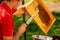 Beekeeper in red t-shirt cuts wax from honeycomb frame with a special knife into a bowl. Honey production. Close up