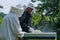 Beekeepers with protective clothes and hats work in apiary on sunny spring day