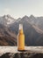 Beer bottle elegantly placed on a flat rock against the breathtaking backdrop of majestic mountains.