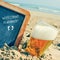 Beer and chalkboard with the text welcome summer, on the sand of