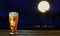 The beer in the glass and the beer foam dripping on the glass on a wooden floor table. Full moon Reflection on the sea at night