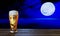 The beer in the glass and the beer foam dripping on the glass on a wooden floor table. Full moon Reflection on the sea at night