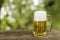 Beer in glass on wooden table with blurred green summer leaves o.