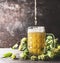 Beer pours into mug on table with fresh hops at dark rustic wall background