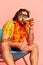 Beer time. Man in summer shirt and short with Hawaiian flower garland on chest posing over pink background. Leisure