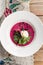 Beet cream cold soup with garlic and sour cream on white plate on wooden table