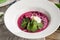 Beet cream cold soup with garlic and sour cream on white plate on wooden table