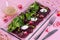 Beetroot salad with boiled goat cheese and greens. Served on a transparent plate on a pink background.