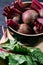 Beets with green tops in round metal pan on dark black wooden background, fresh red beetroot on backdrop kitchen table top view