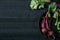 Beets with green tops in round metal pan on dark black wooden background, fresh red beetroot on backdrop kitchen table top view