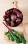 Beets with green tops in round metal pan on natural wooden background, fresh red beetroot on backdrop kitchen table top view