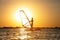 A beginner windsurfer woman stands on a board with a sail on a sunset background. Windsurfing school