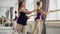 Beginning ballet dancers are lerning to raise leg backward holding ballet barre while serious teacher is giving