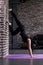 Beginning female yogi practicing yoga inversion poses standing on hands upside down leaning against wall in fitness club