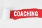 Behind torn white paper on a red background, the text - COACHING