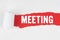 Behind torn white paper on a red background, the text - MEETING