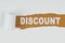 Behind torn white paper on a wooden background the text - DISCOUNT